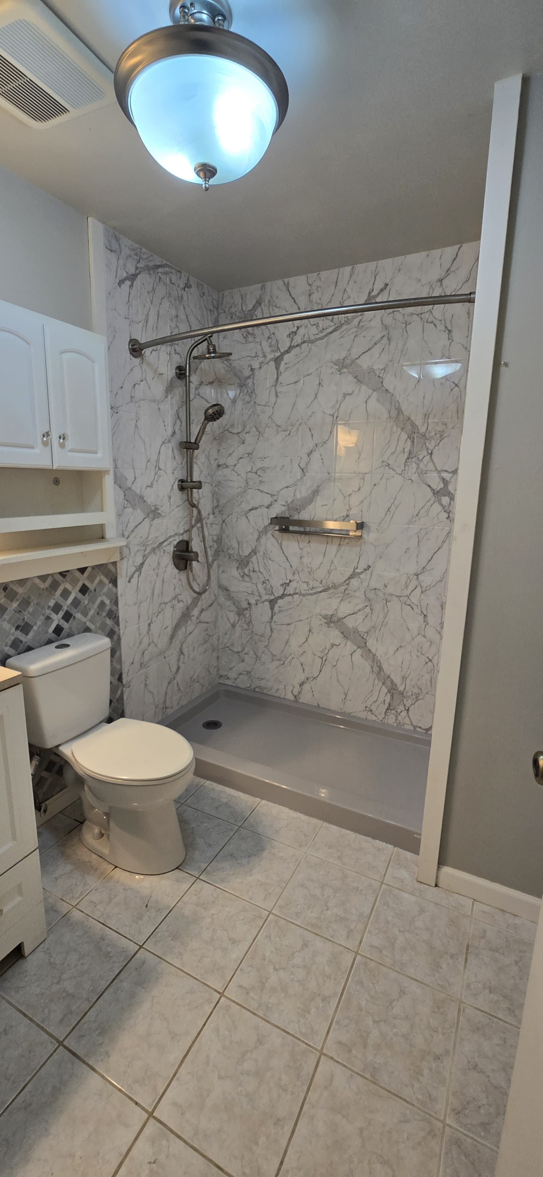 Modern bathroom with marble-look shower enclosure, white toilet, storage cabinets, and ceiling light fixture