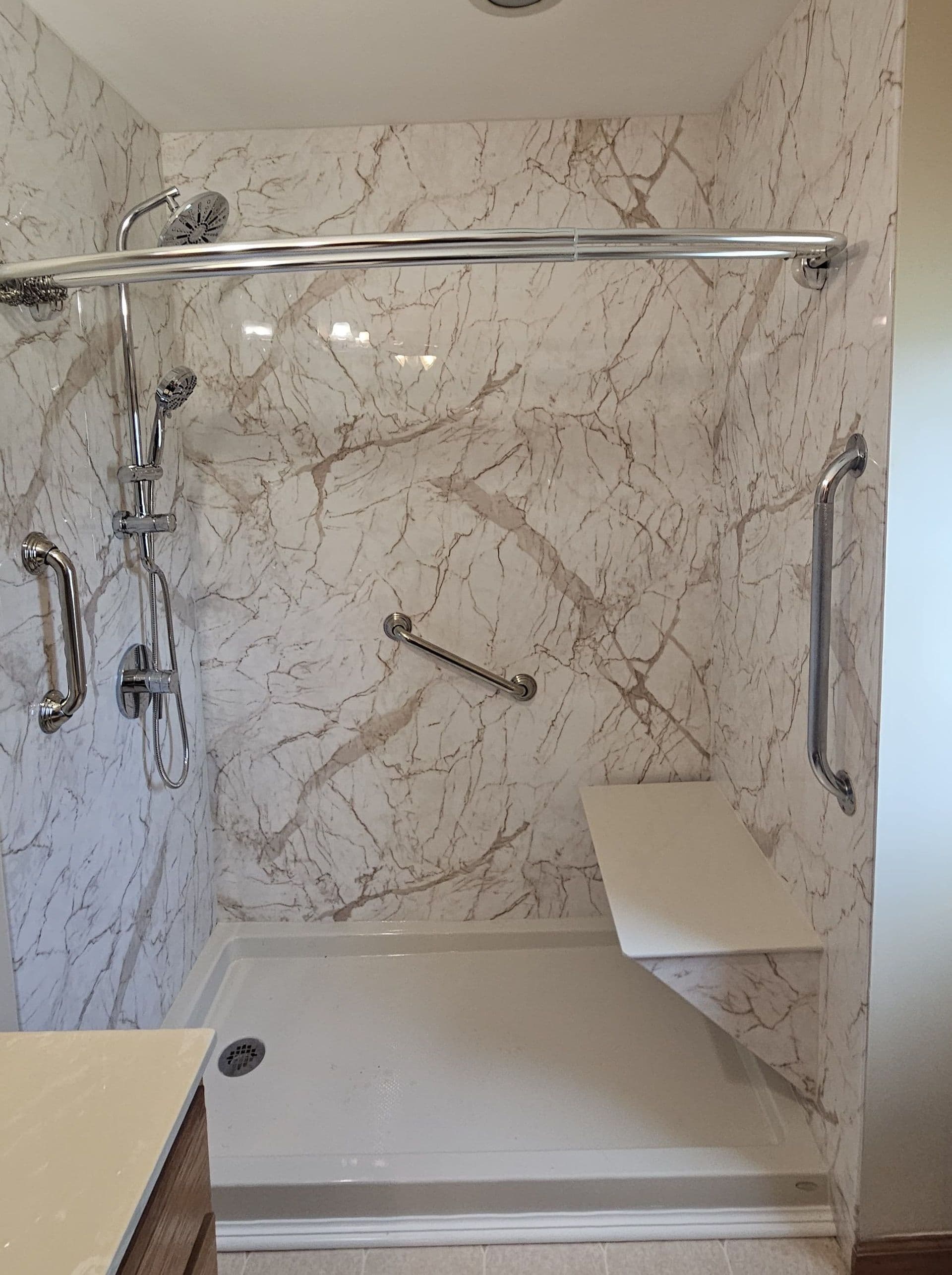 Marble-clad walk-in shower with chrome fixtures, rainfall showerhead, handrails, and built-in bench seat