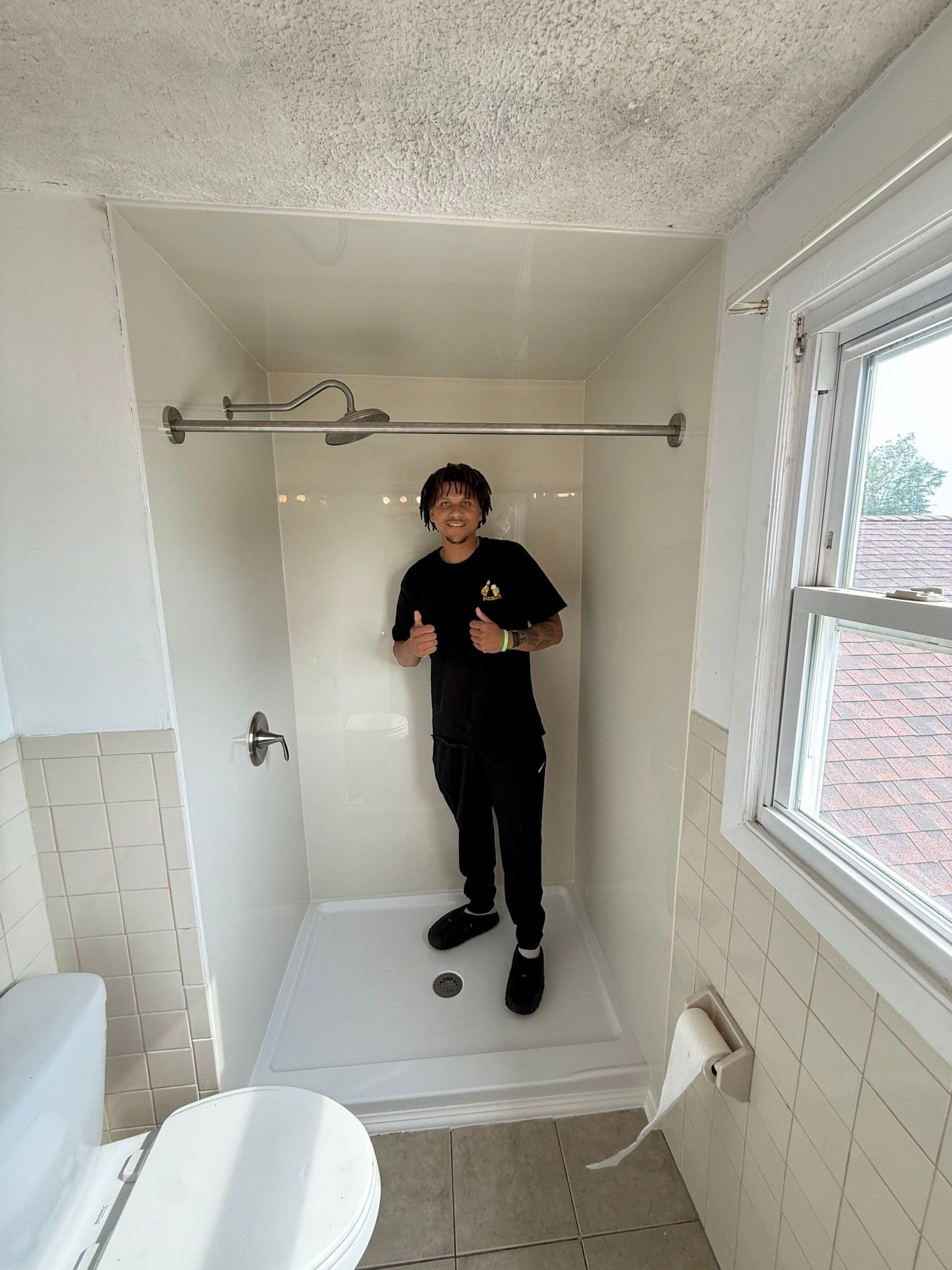 Person giving thumbs up inside a newly renovated shower stall with white tile walls and chrome fixtures
