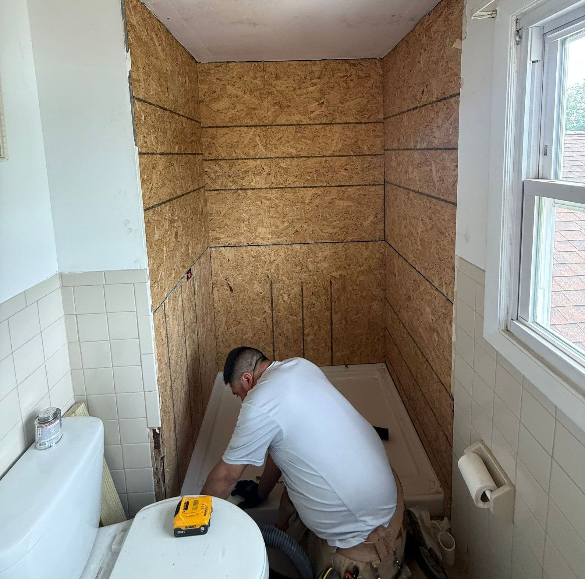 Worker installing shower enclosure with OSB board framing in bathroom renovation