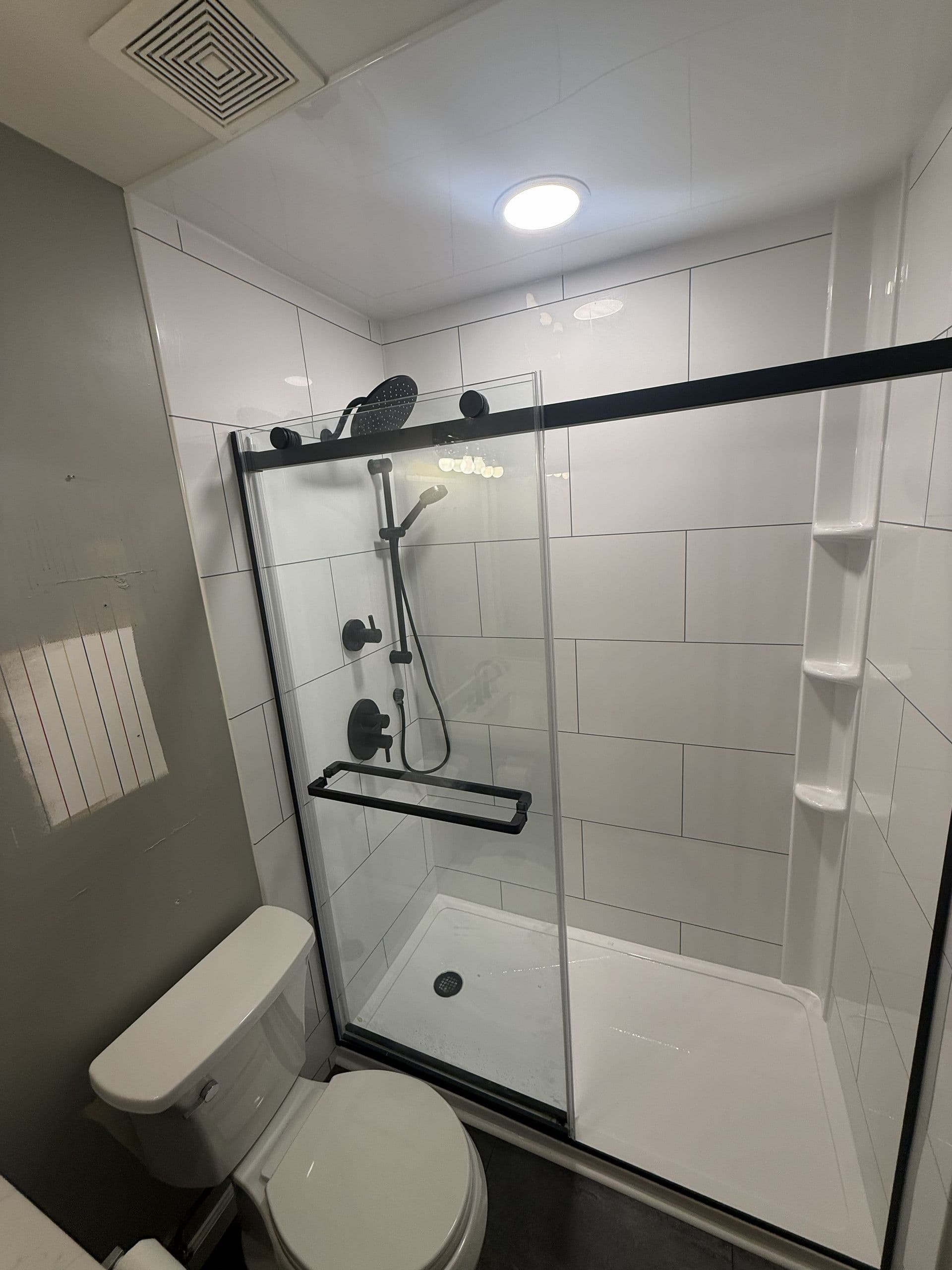 Modern bathroom with walk-in shower enclosure featuring black frame and fixtures, white subway tile walls, overhead rainfall showerhead, toilet, and built-in shelving