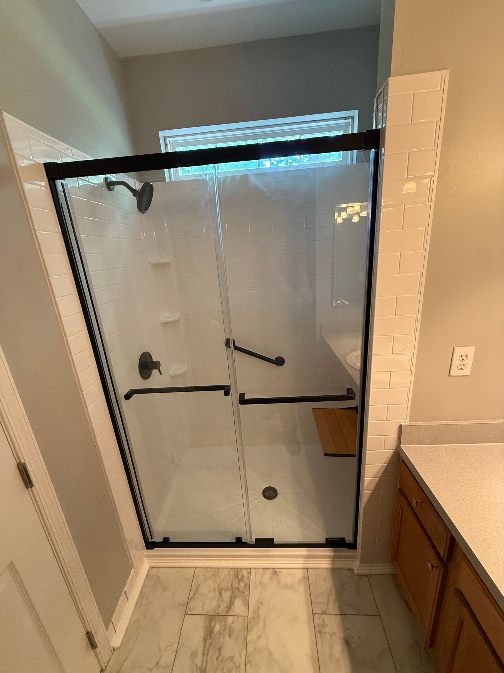 Frameless glass shower enclosure with black metal framing and sliding doors installed in a modern bathroom with tile walls and flooring