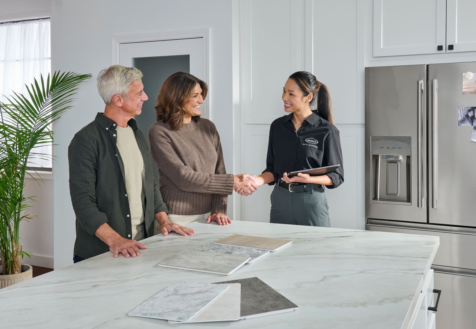 A couple shakes hands with a representative as they look over tile samples.